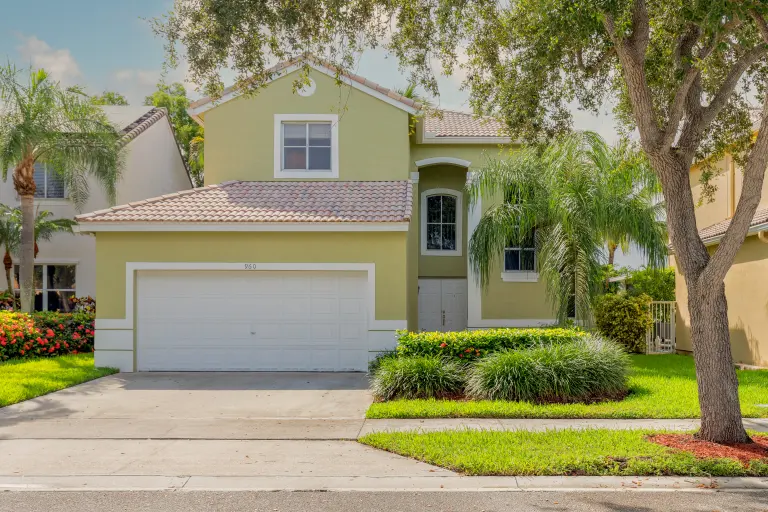 Two story stucco home with a tile roof, white garage door and palm trees