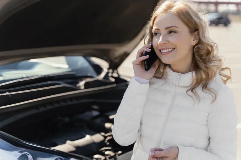 Woman talking on her phone beside a car with the hood open