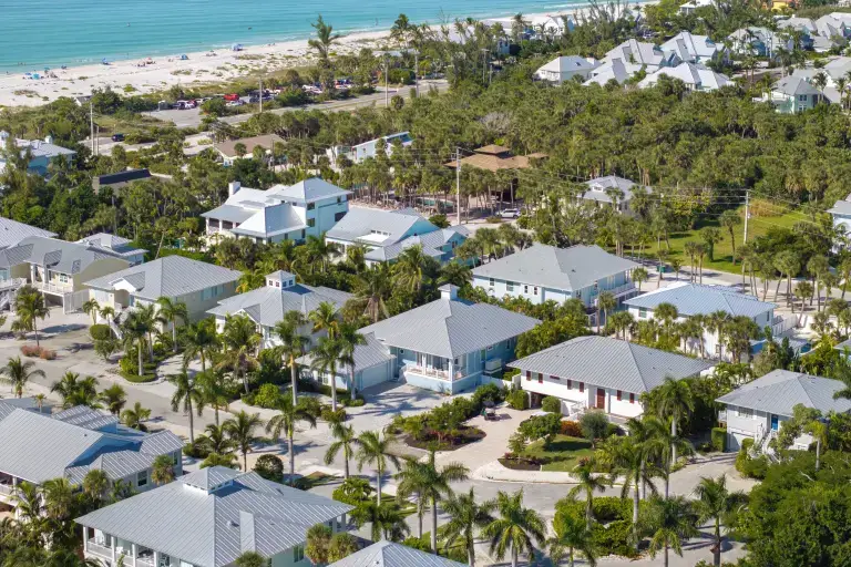 Aerial view of coastal homes with metal roofs among palm trees near the beach
