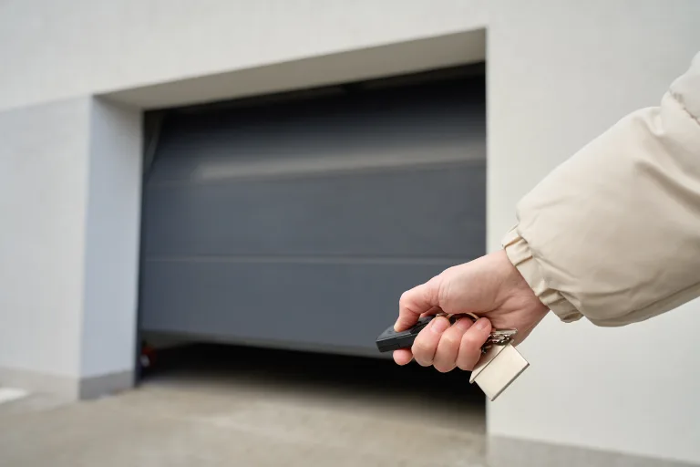 Hand pressing a garage door remote in front of a closed door