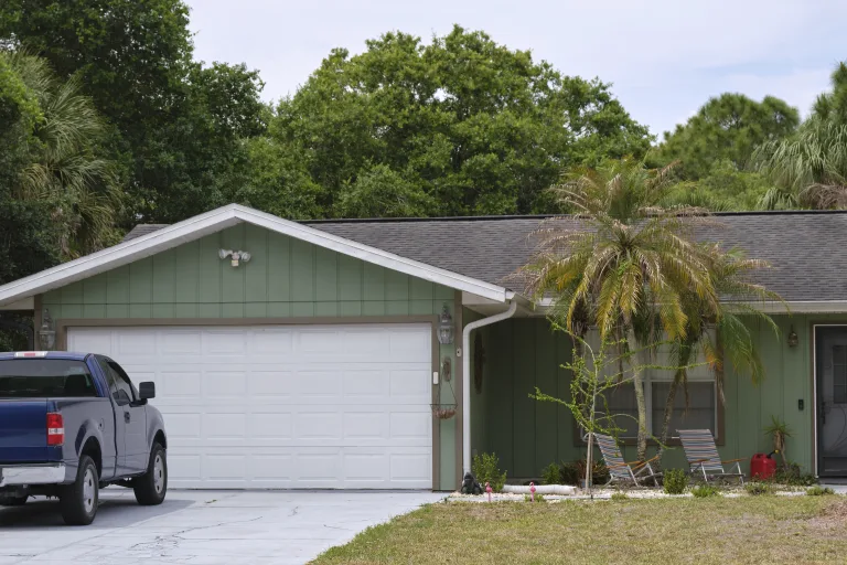 Pickup truck parked beside a white double garage door on a single story home
