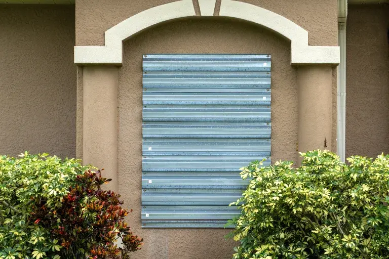 Corrugated steel storm shutter covering a window on a stucco home